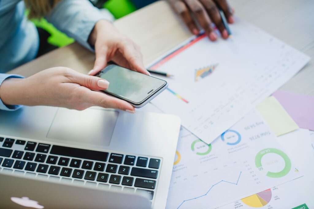 Analyse de données sur ordinateur portable, smartphone à la main, avec graphiques et rapports financiers.